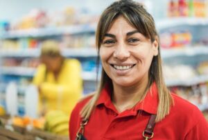 Female retail worker wearing a red polo shirt standing in front of stocked shelves