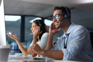 two people speaking on headsets and working on computers