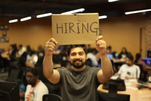 man at a workplace holding a sign that says "hiring"