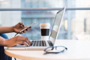 person using a mobile phone and typing on a laptop