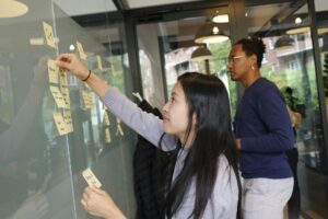 one woman writing and pasting post-it notes on a wall 